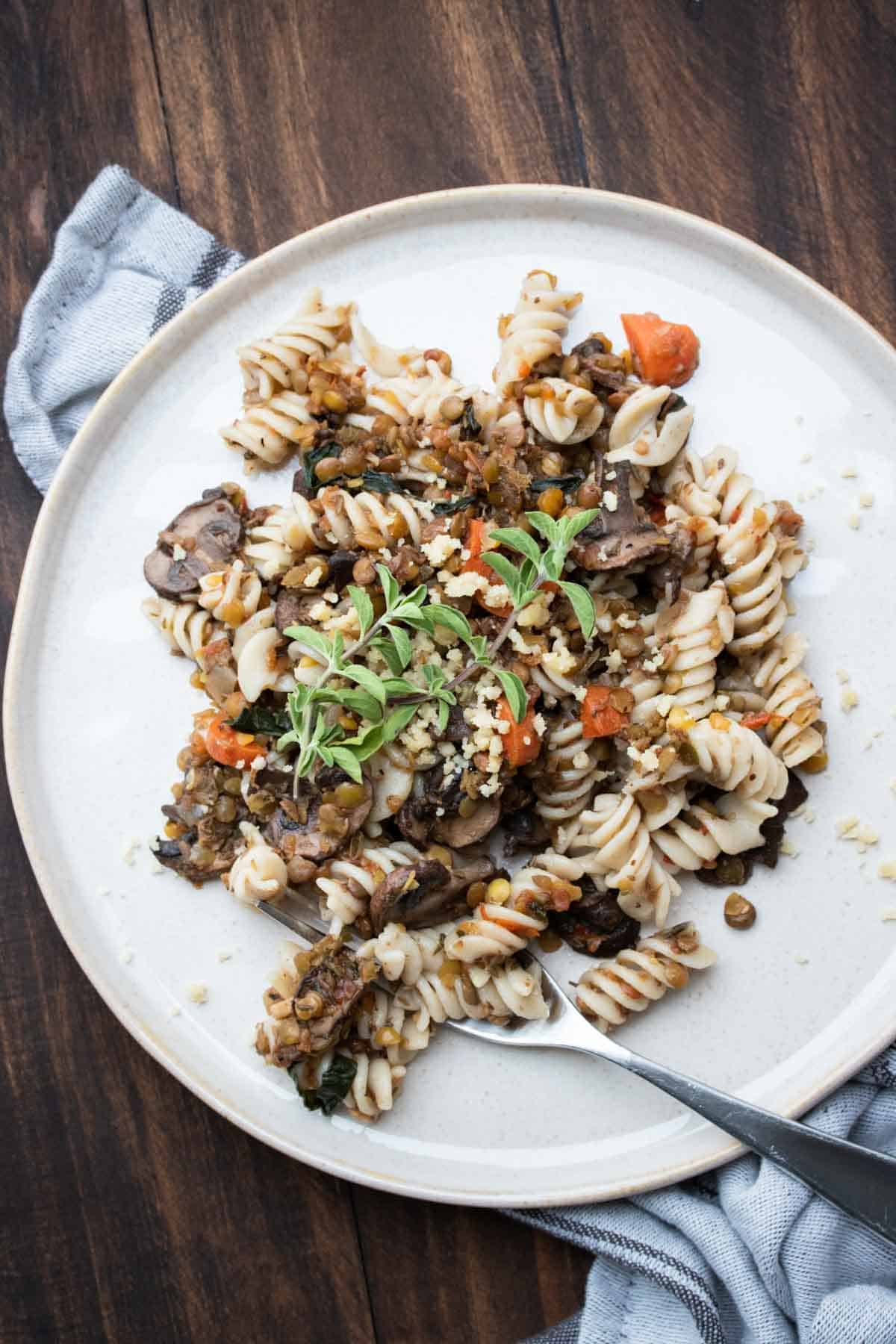 White plate with rotini pasta and lentil bolognese on it.