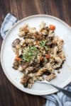 A fork in a pile of spiral pasta mixed with lentil bolognese and on a cream plate.