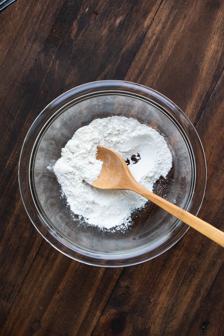 Top view of wooden spoon mixing flour in a glass bowl