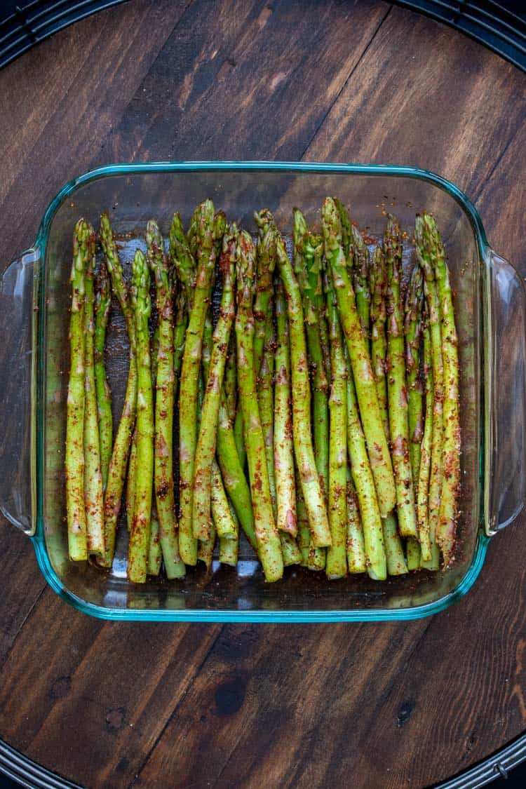 Asparagus spears covering in sprinkled paprika in a glass baking dish