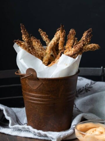 Crispy breaded asparagus fries wrapped in parchment in a brown bucket