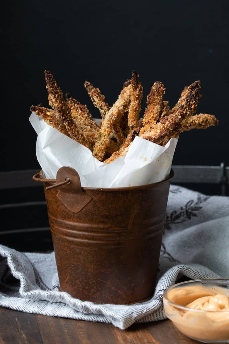 Crispy breaded asparagus fries wrapped in parchment in a brown bucket