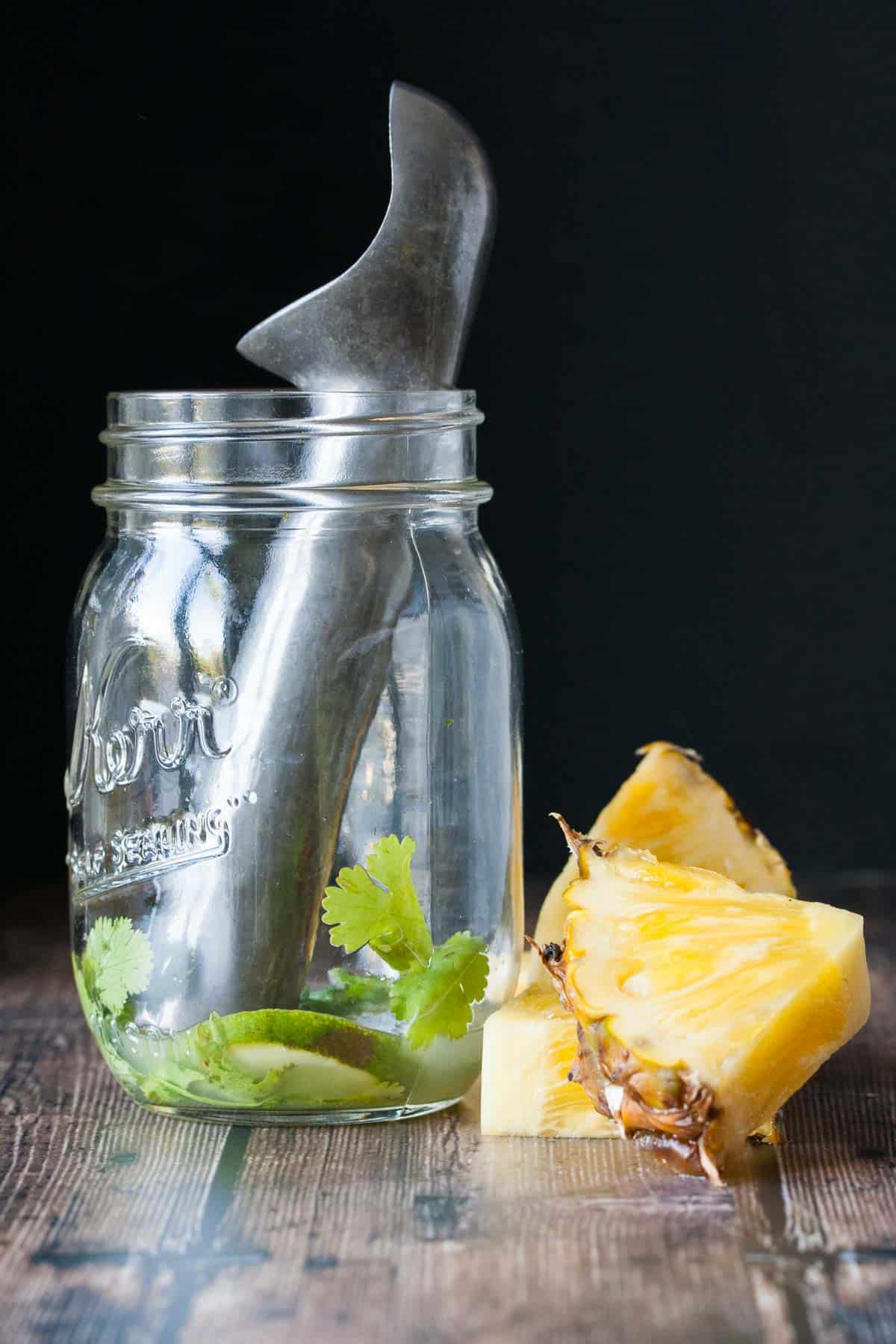 Muddling cilantro, lime juice, jalapeño and tequila in a glass jar