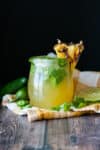 A glass jar filled with a pineapple jalapeño margarita on a yellow checkered towel next to a jalapeño and lime slice