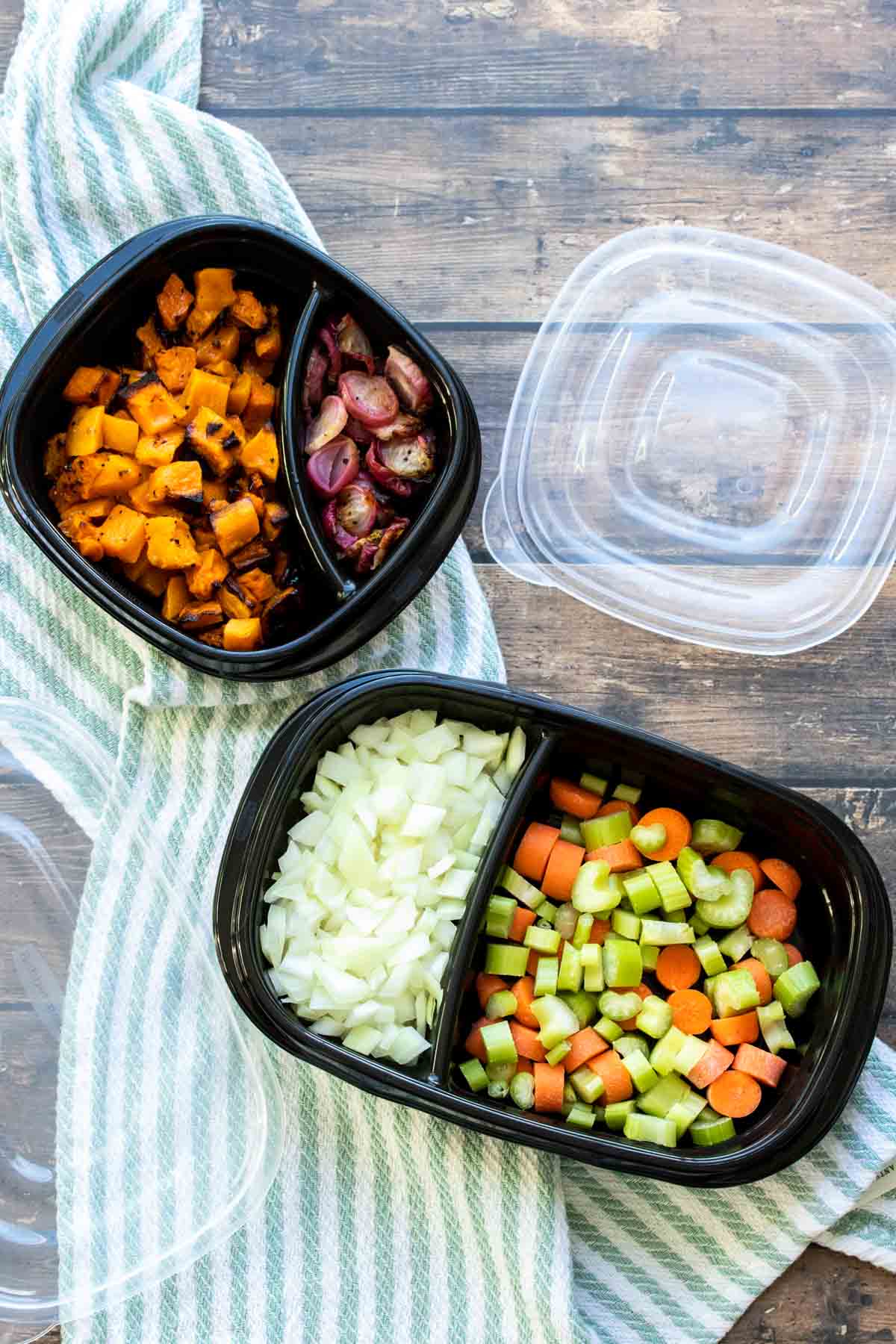 Black containers with compartments filled with raw chopped veggies.