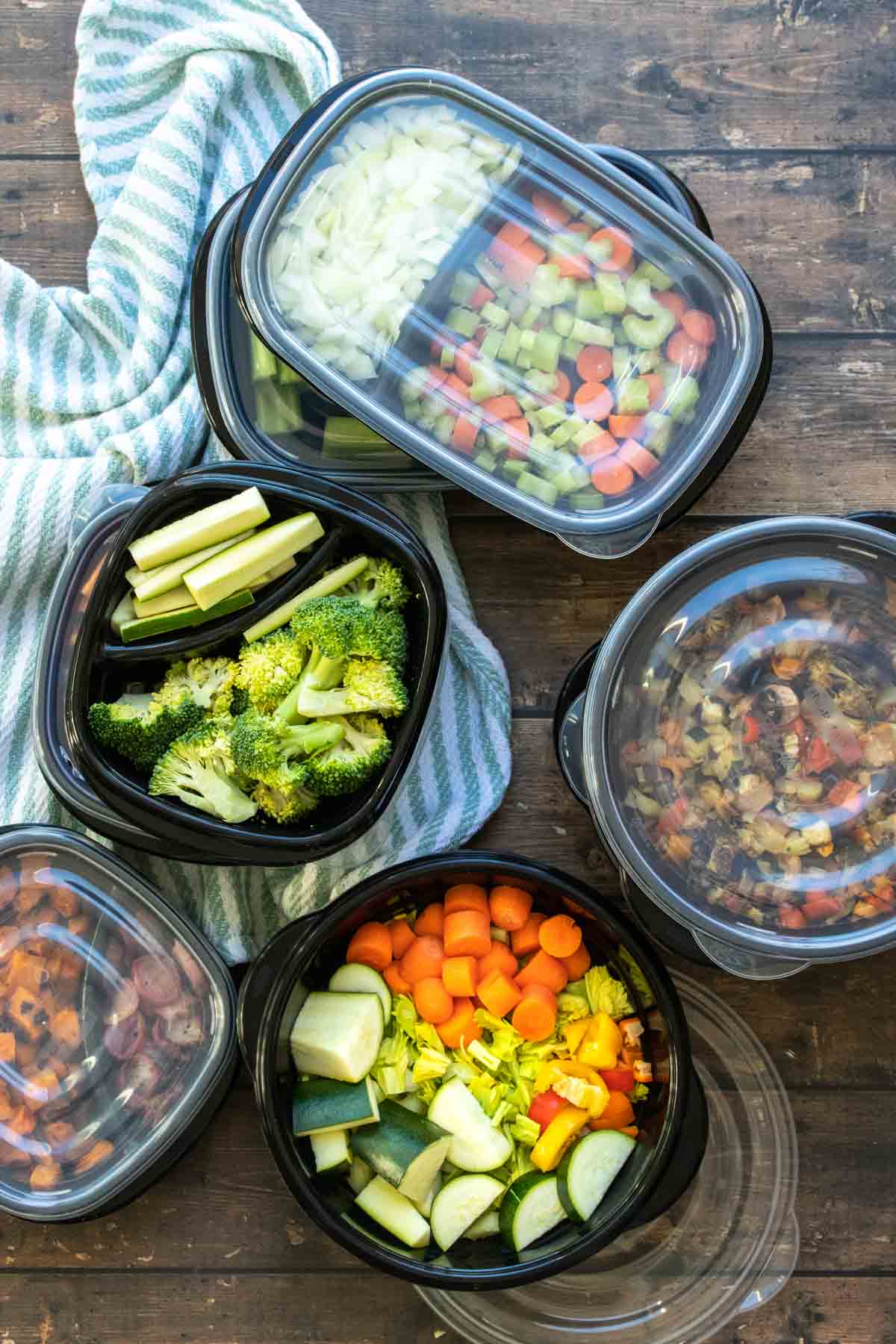 Black containers, some with lids on, filled with chopped veggies.