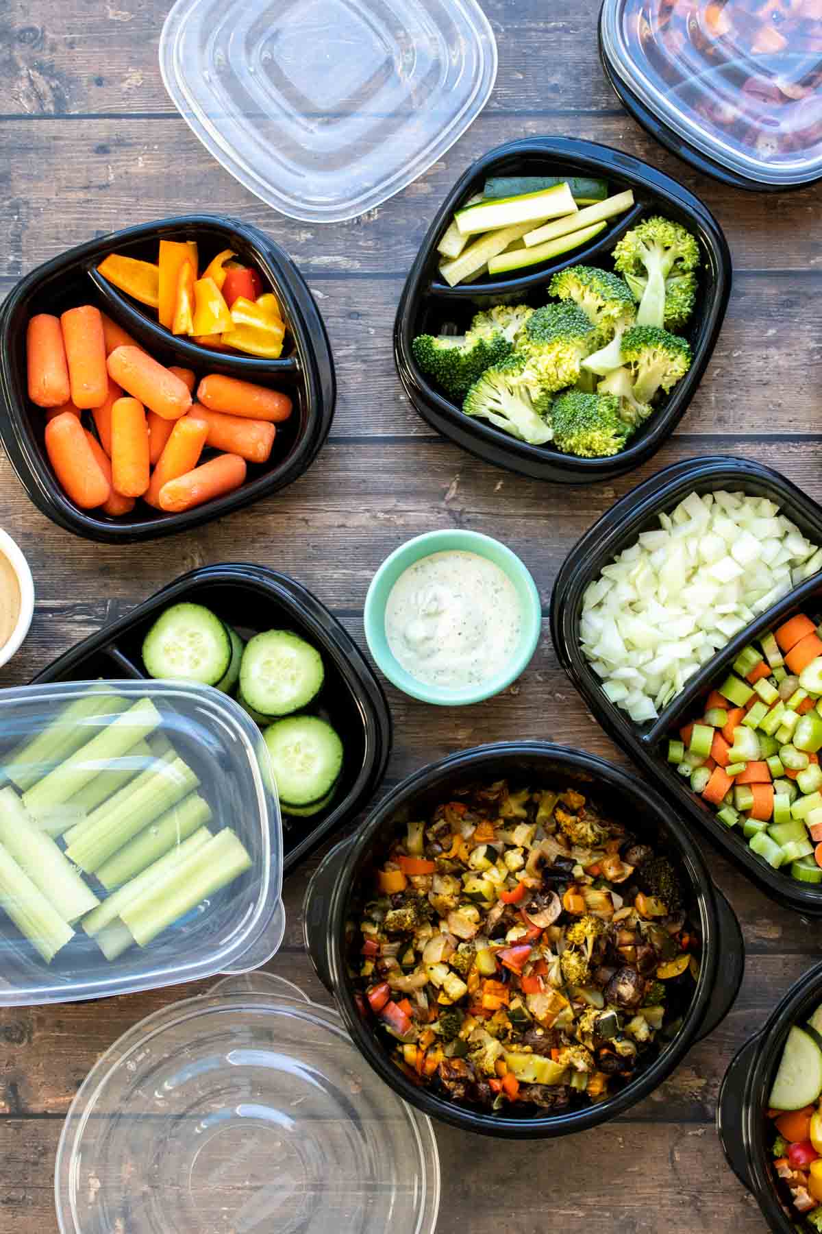 Black containers filled with chopped veggies on a wooden surface.