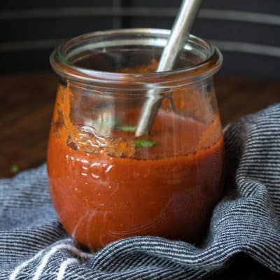 Glass jar with red enchilada sauce inside and a spoon in it