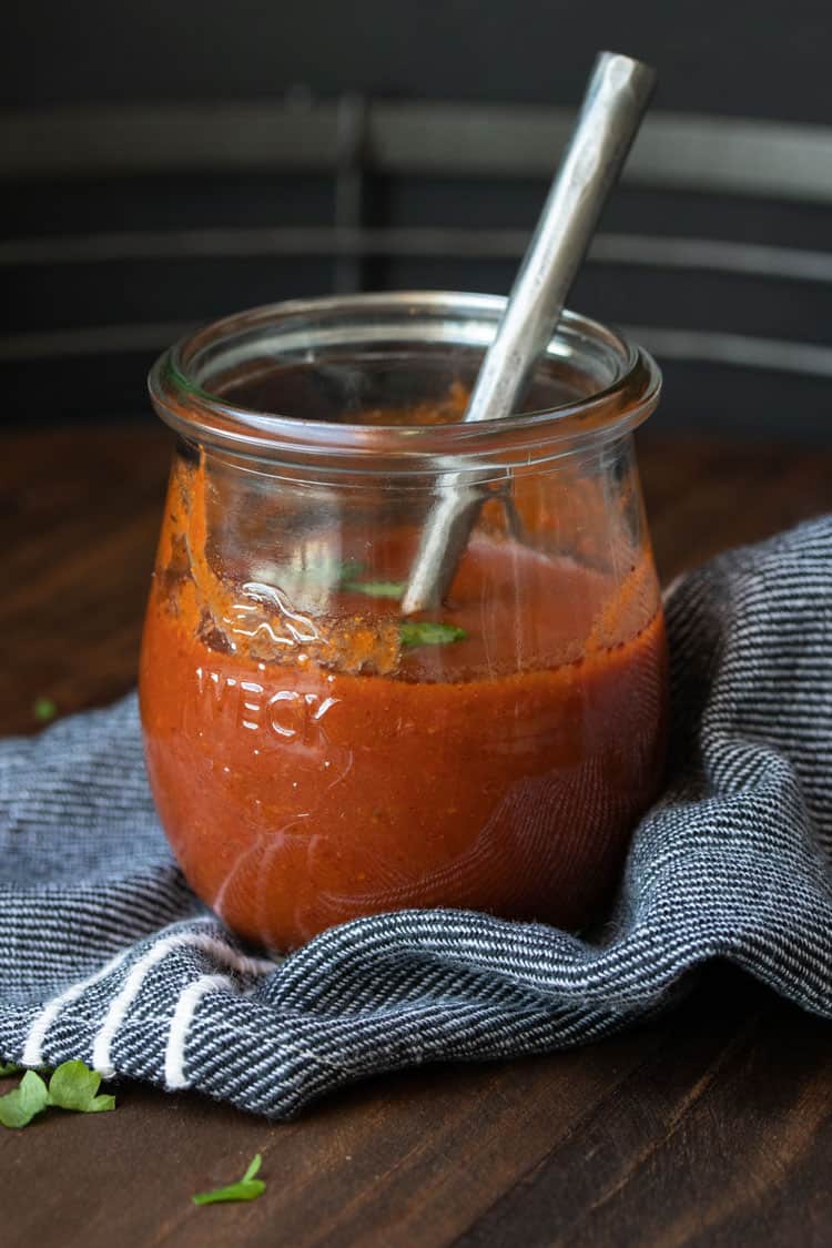 Glass jar with red enchilada sauce inside and a spoon in it