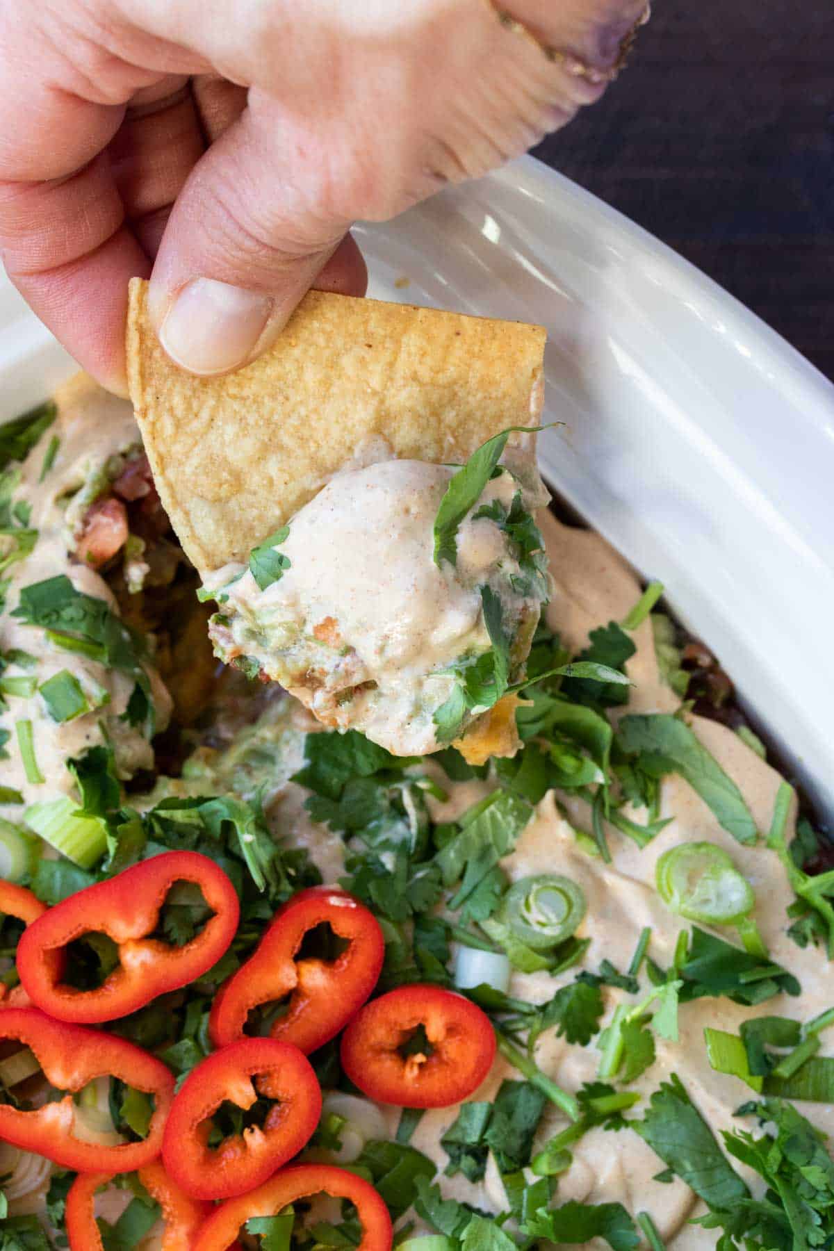 Hand dipping tortillas chip into a dish of 7 layer dip