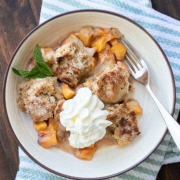 Peach cobbler with whipped cream in a cream bowl