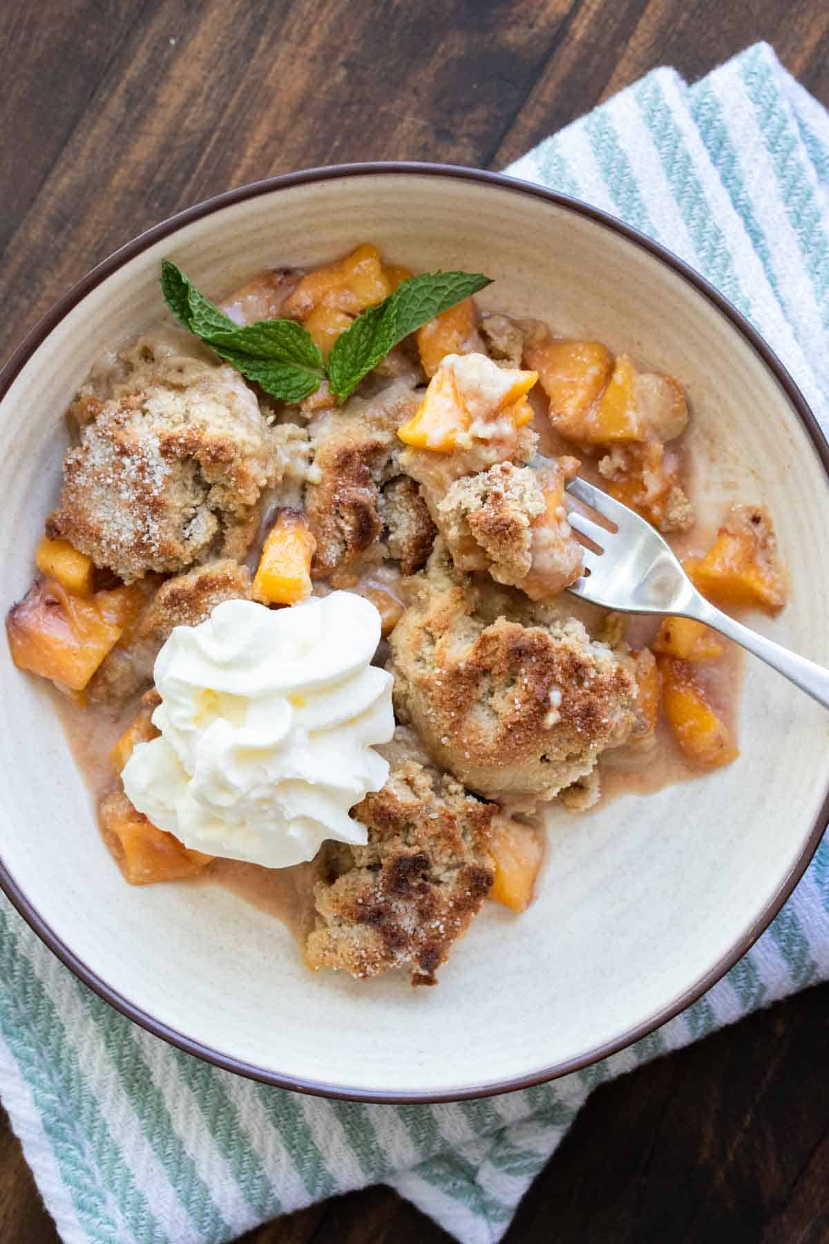 Fork taking a bite of peach cobbler from a cream bowl.