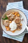 A shallow cream bowl with brown edge with a serving of peach cobbler in it topped with whipped cream and a mint leaf.