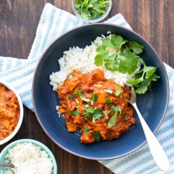 Black plate with sweet potato red curry over white rice with a cilantro sprig