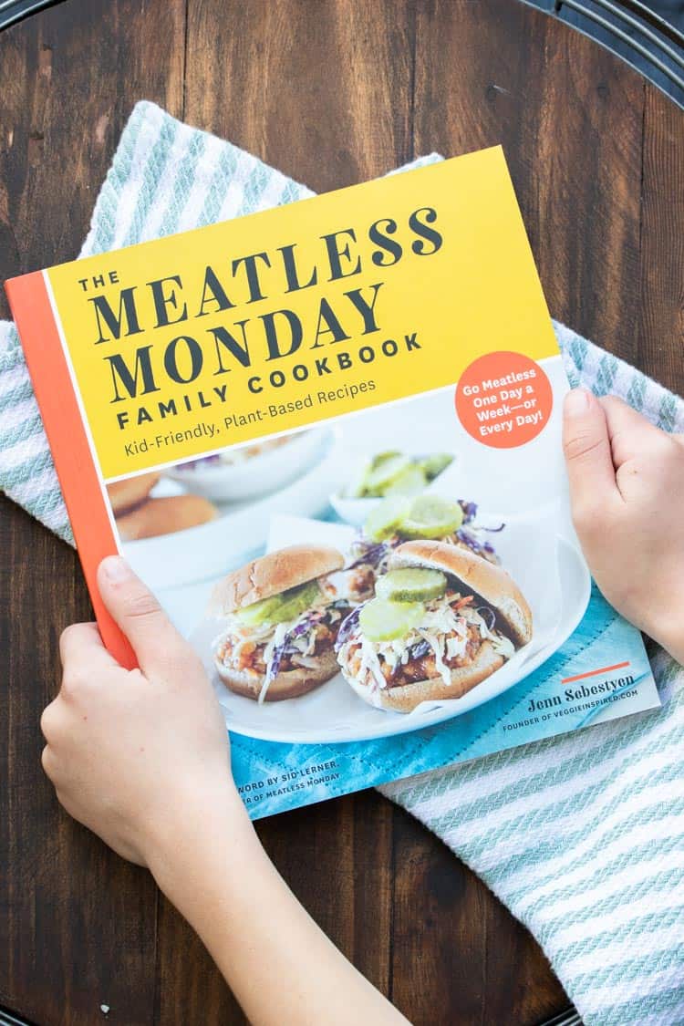 Hands holding a meatless monday cookbook with lentil sloppy Joe's on the cover