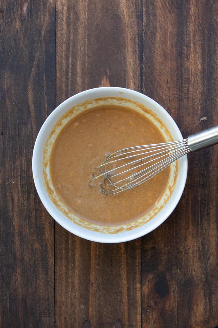 Whisk mixing peanut sauce in a white bowl