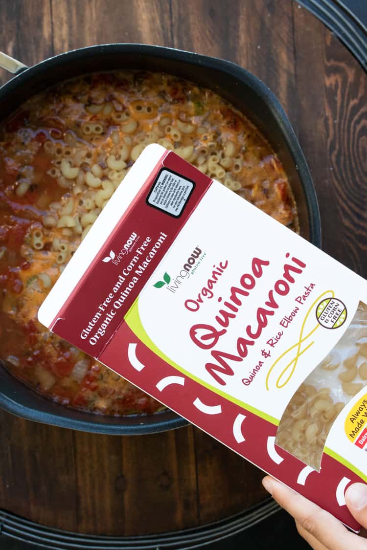 Hand pouring box of quinoa macaroni into a pot of soup