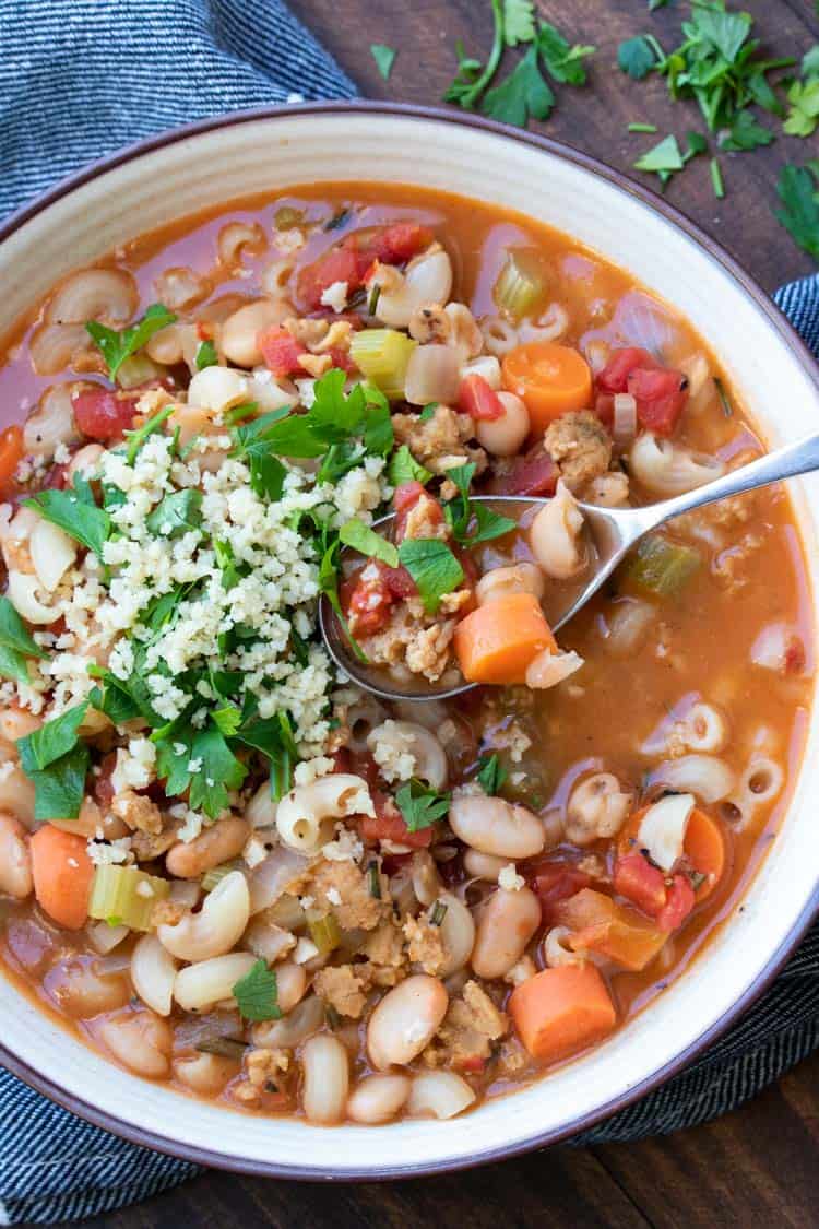 Spoon getting a bite of vegetable pasta fagioli soup from a white bowl