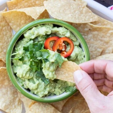 Hand dipping a tortilla chip into a bowl of guacamole