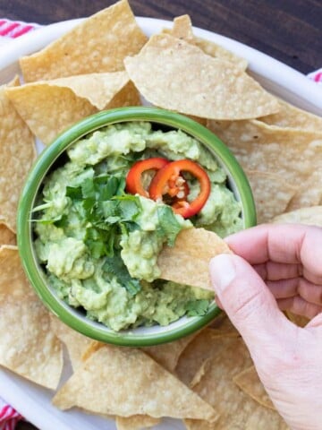 Hand dipping a tortilla chip into a bowl of guacamole