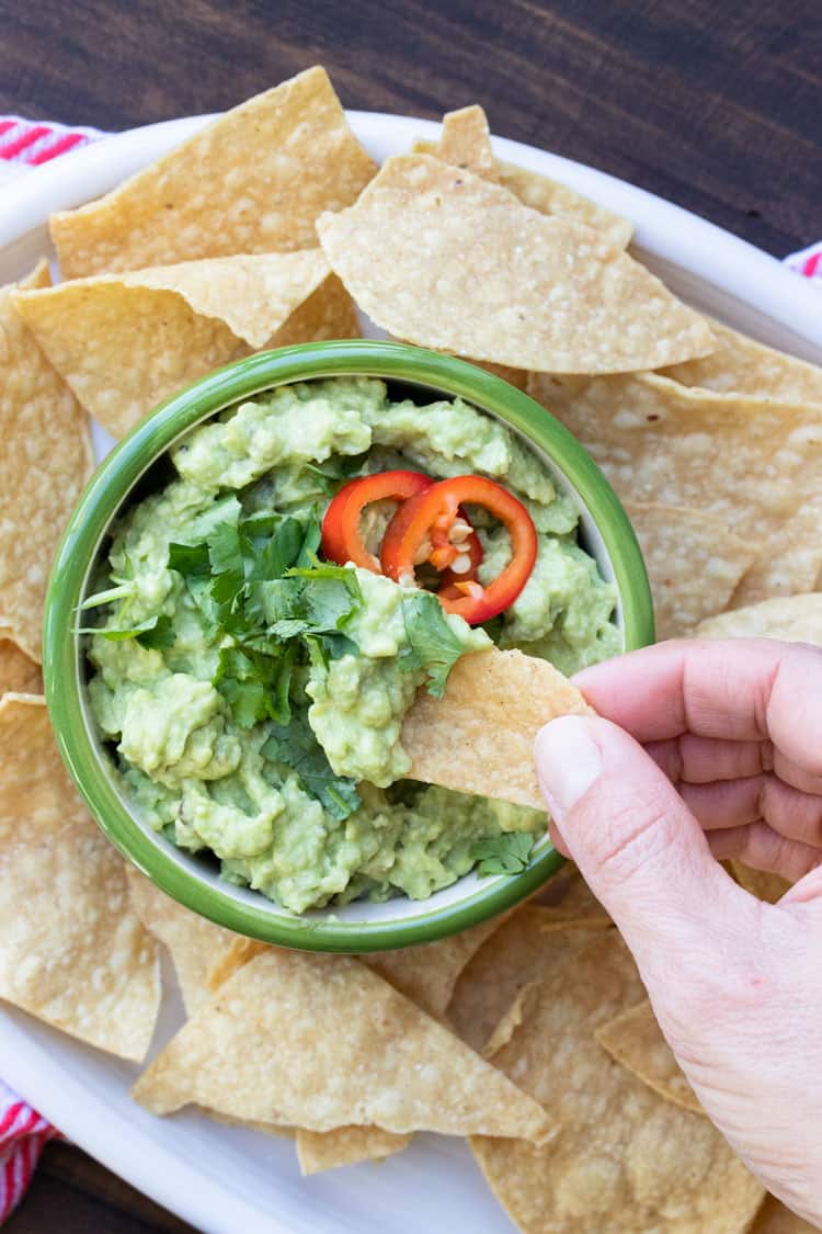 Hand dipping a tortilla chip into a bowl of guacamole