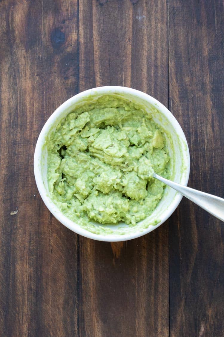 Mashed avocado in a white bowl with a fork in it