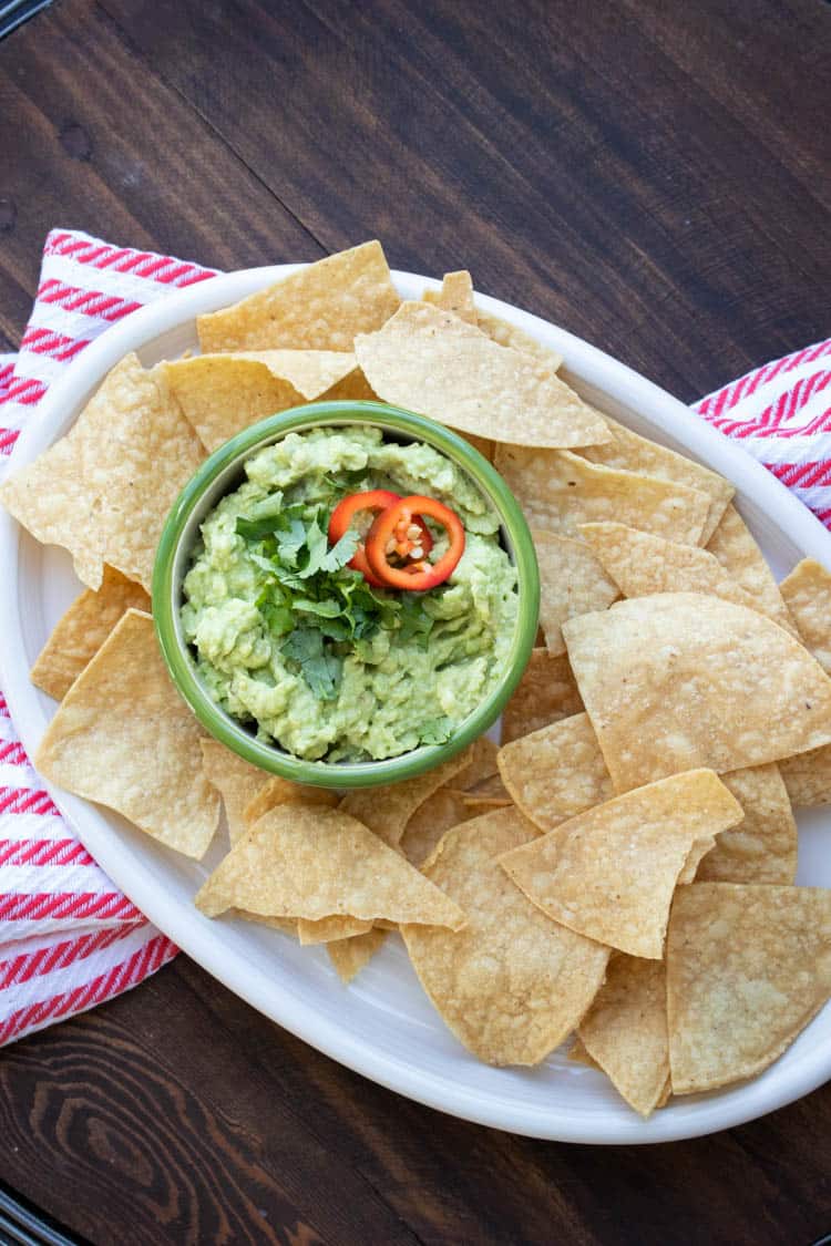 White platter with tortilla chips around a bowl of guacamole