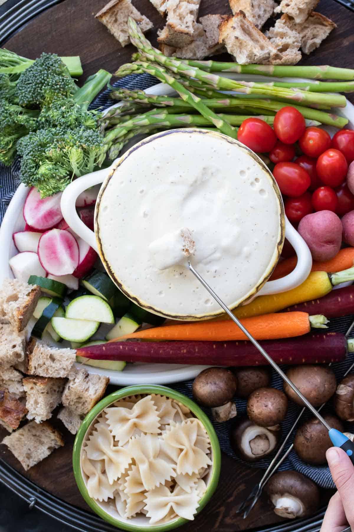 Fondue fork with a piece of bread dipping into bowl of white cheese fondue.