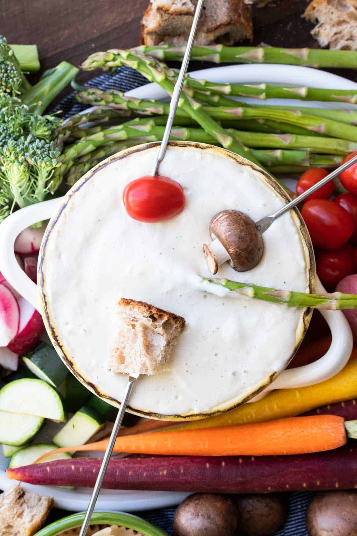 Four fondue forks with veggies dipping into a bowl of cheese fondue.