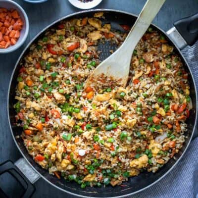 Rice and veggies being cooked in a pan and mixed with a wooden spoon