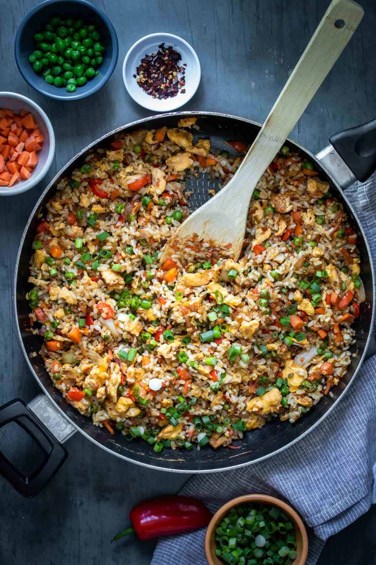 Rice and veggies being cooked in a pan and mixed with a wooden spoon