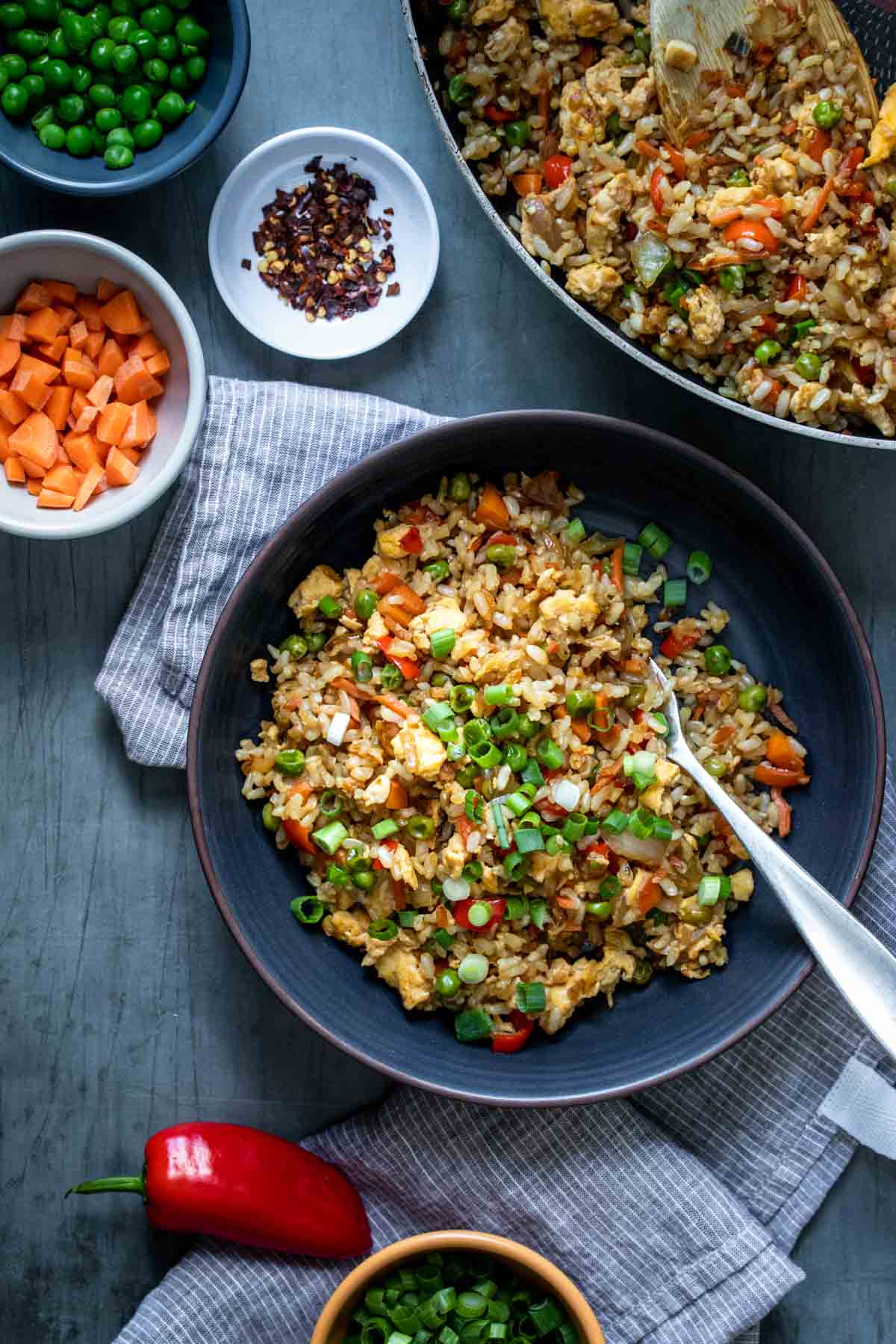 Dark plate with veggie fried rice and a fork in it on a striped towel