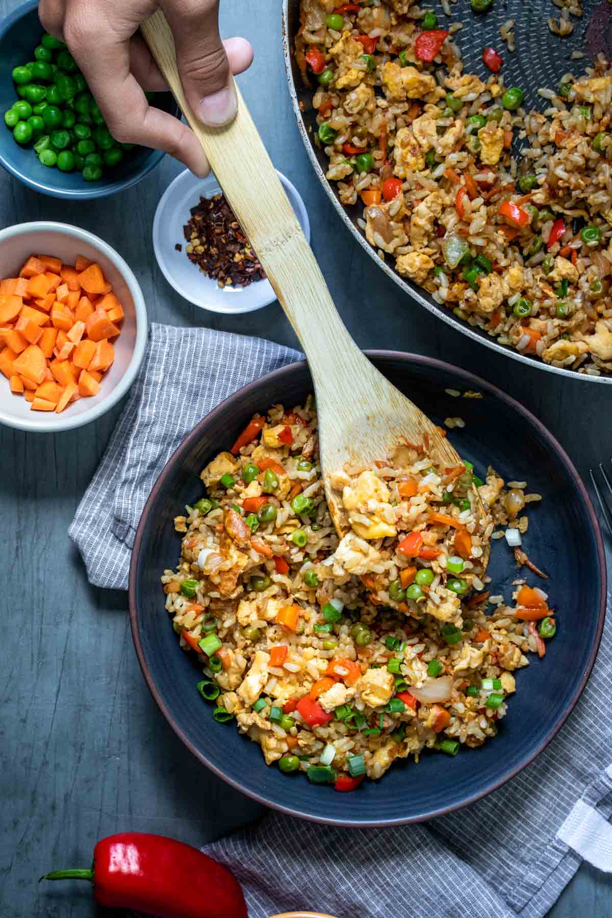 Wooden spoon serving fried rice onto a dark plate