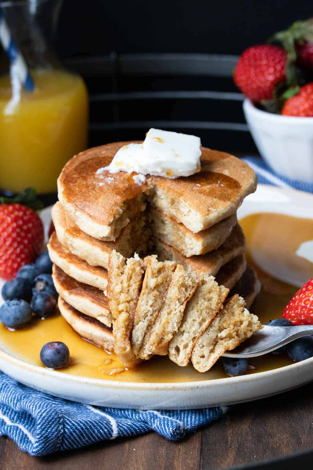 Bite from a stack of pancakes on a fork laying down on a white plate with maple syrup