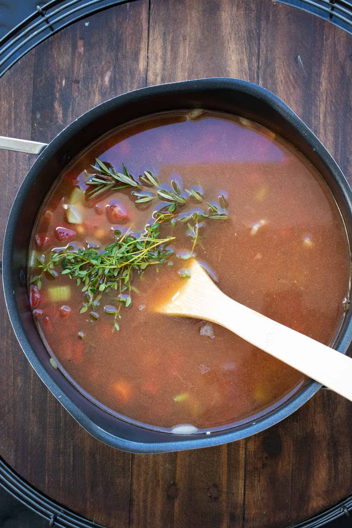 Veggie and bean soup in a pot with sprigs of rosemary and thyme on top