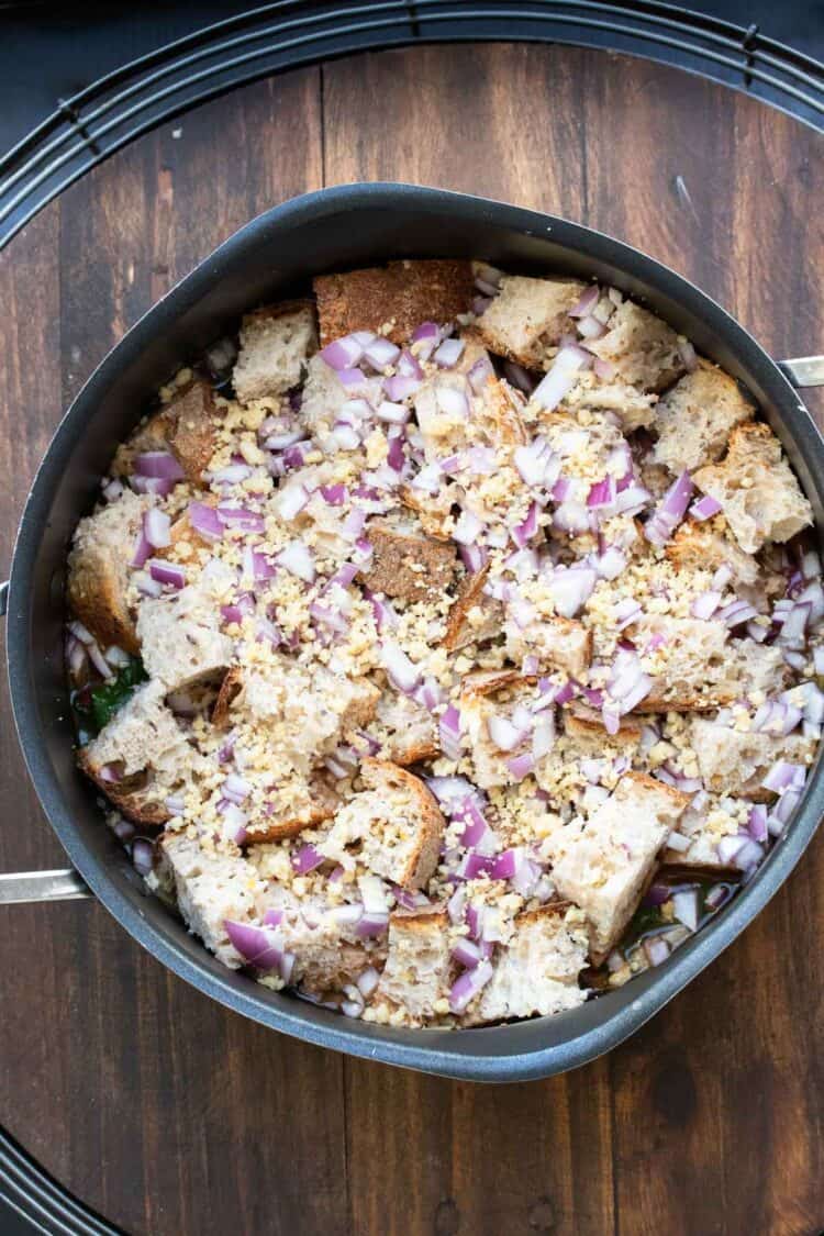 Bread cubes and chopped red onion on top of soup in a pot