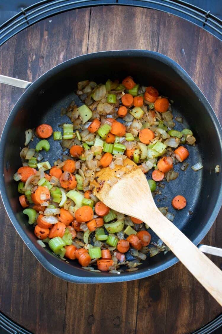 Wooden spoon sautéing veggies in a pot.