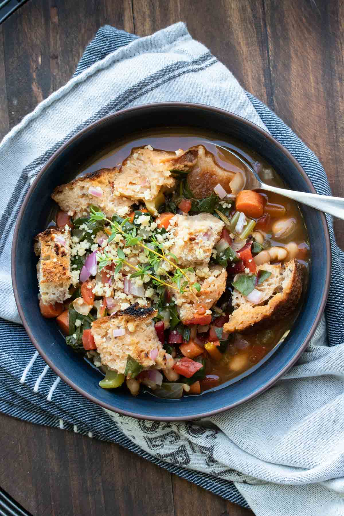 Black bowl of veggie and bean soup with bread cubes and fresh herbs on top