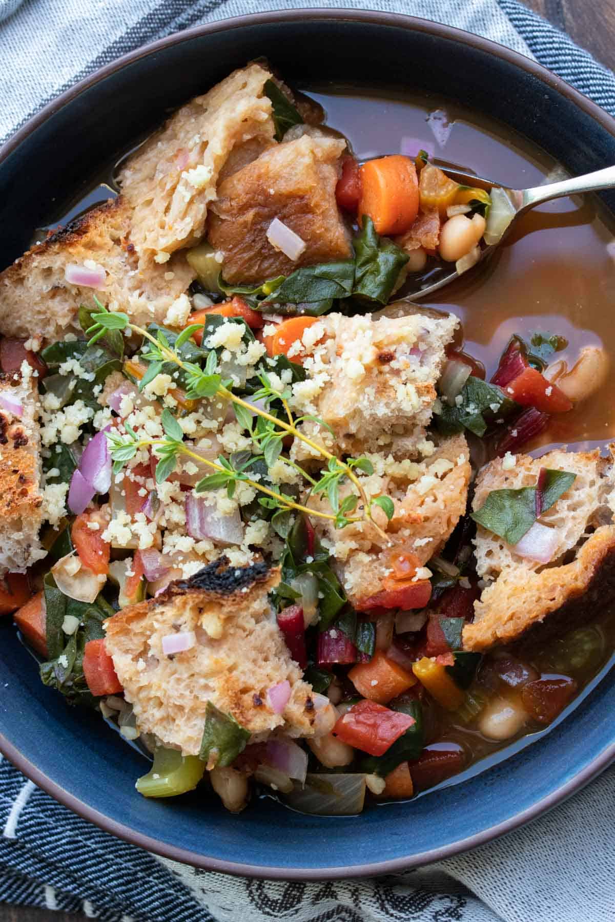 Spoon getting a bite of veggie and bean bread soup from a black bowl.