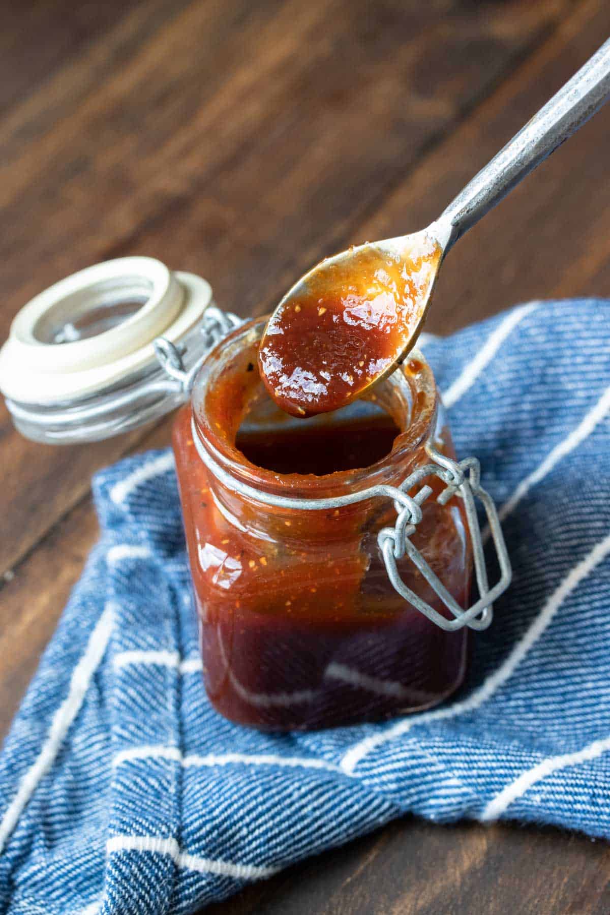 A spoon getting a scoop of steak sauce from a glass jar.