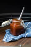 A hinged glass jar filled with a red sauce on a blue towel with white stripes and a metal spoon in it.