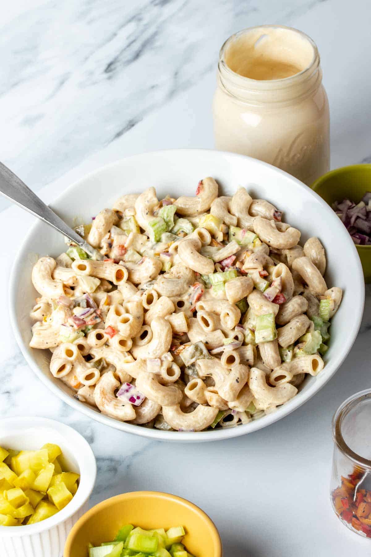 Spoon mixing creamy macaroni salad ingredients together in a white bowl.
