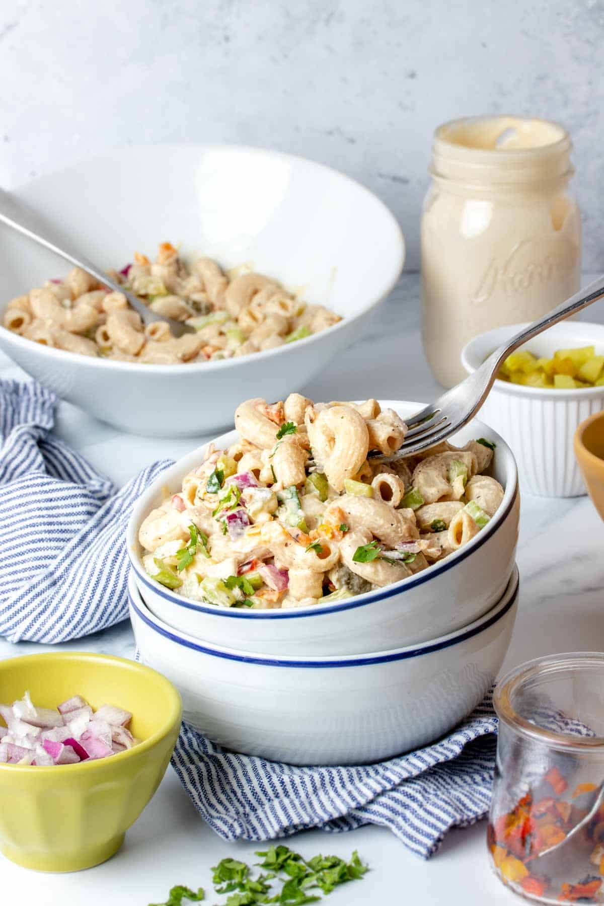 Two white bowls stacked and filled with creamy macaroni salad and a fork getting a bite from it.