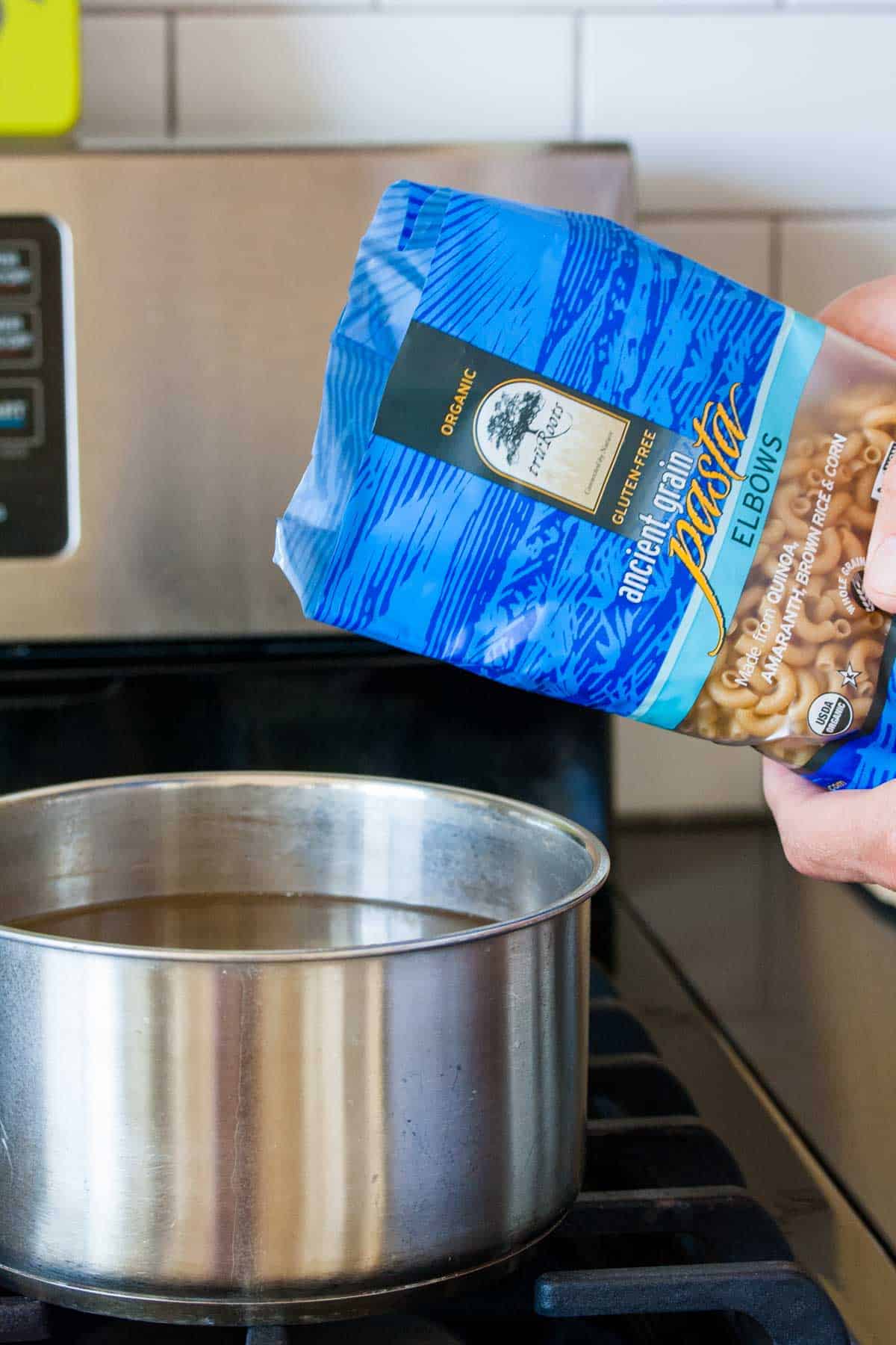 Hand pouring a blue bag of pasta into a pot of water