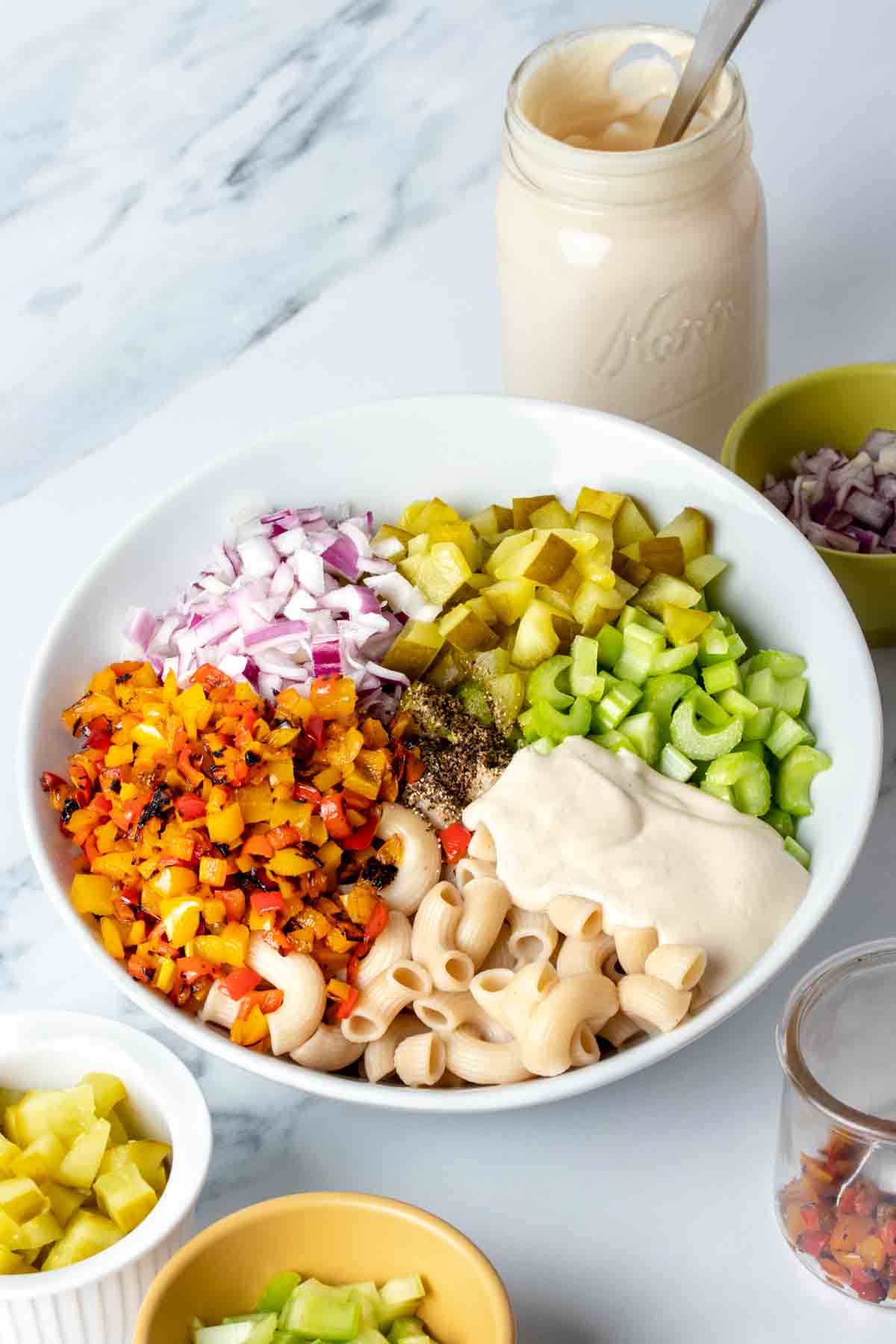 White bowl with ingredients for creamy macaroni salad piled in sections.