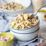 A fork getting a bite of creamy macaroni salad from a stack of two white bowls with blue rims.