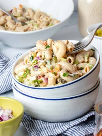 A fork getting a bite of creamy macaroni salad from a stack of two white bowls with blue rims.