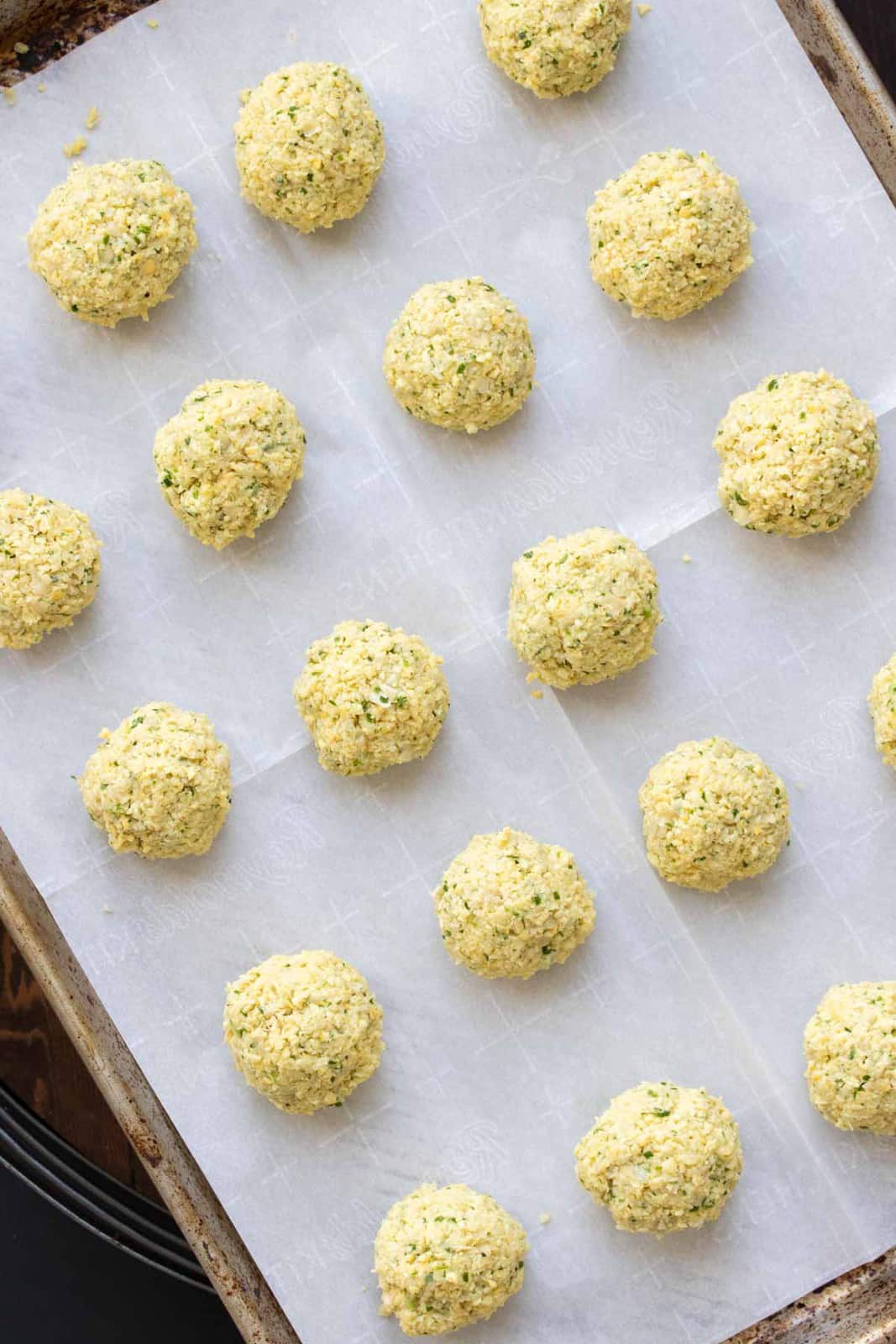 Balls of raw falafel mixture on a parchment lined baking sheet