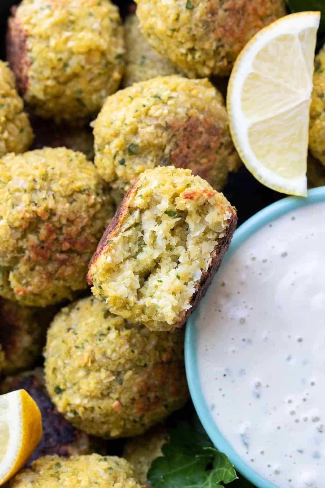 Close up of a half eaten falafel next to a bowl of tahini sauce