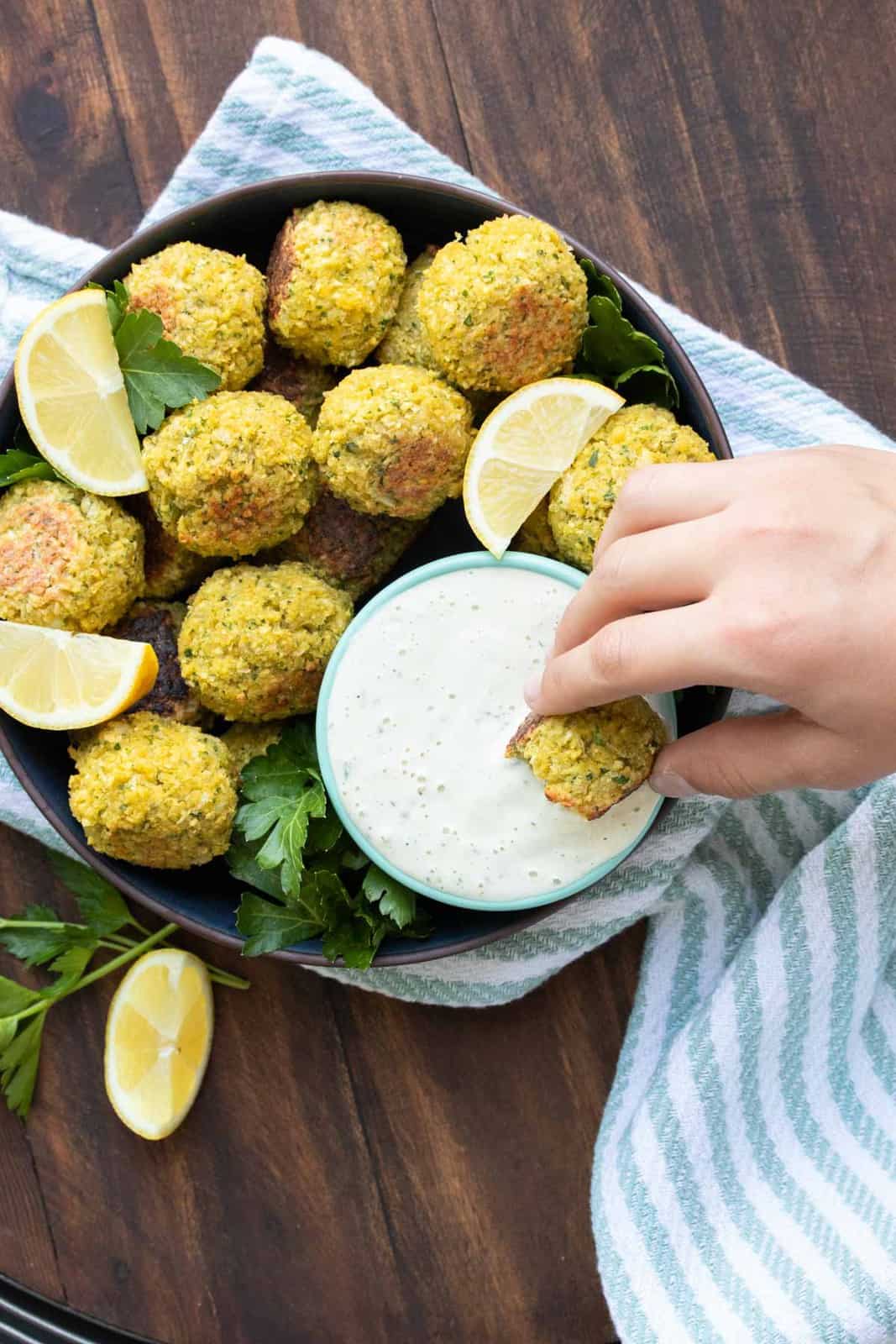 Hand dipping a falafel into a bowl of tahini sauce